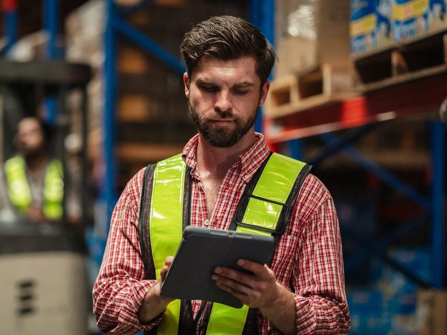 Lucrător de depozit cu tabletă între rafturi înalte