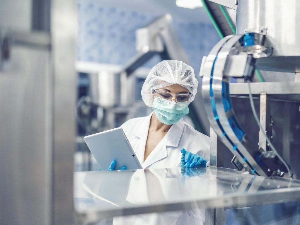 Operator în echipament de protecție, cu tabletă, lângă utilajul de fabricație