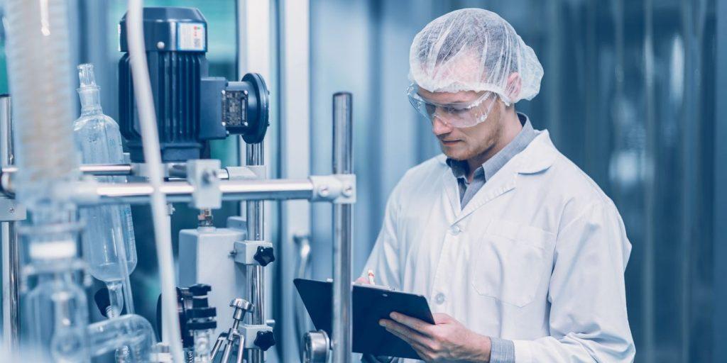 Specialist în producție farmaceutică cu tabletă, lângă linia de producție