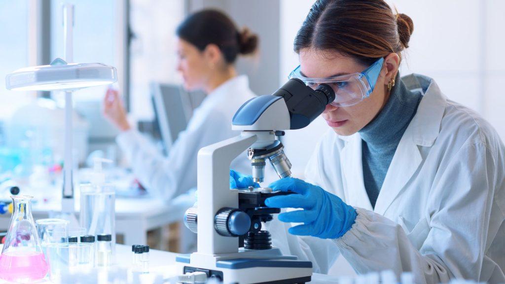 Cercetătoare la microscop, într-un laborator de control al calității