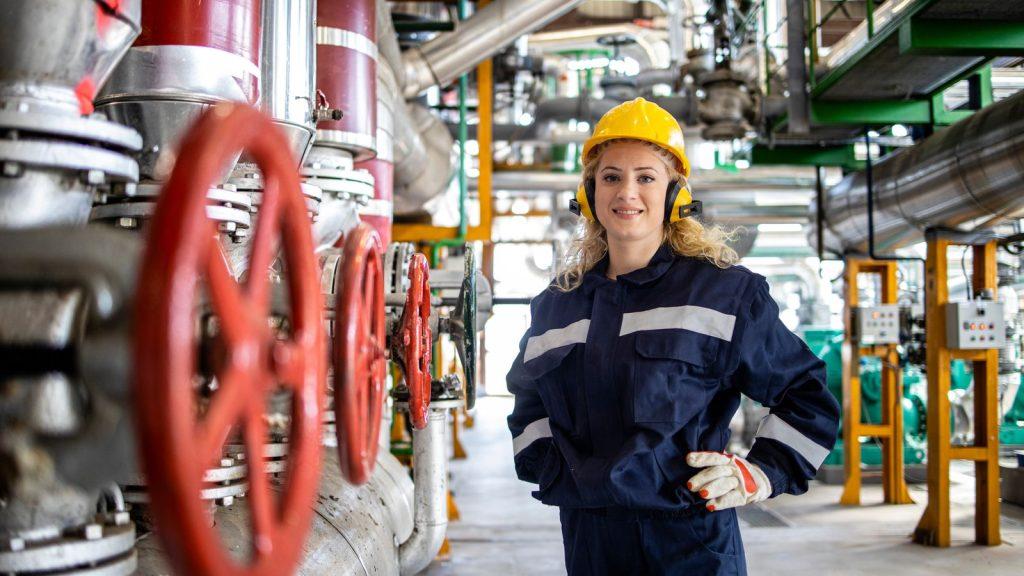 Tehniciană în echipament de protecție lângă robinetele unei instalații industriale